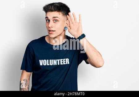 Jeune garçon caucasien avec des oreilles dilatation portant t shirt volontaire sourire avec la main sur l'oreille écouter une audition à la rumeur ou des potins. Concept de surdité. Banque D'Images