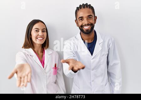 Les jeunes médecins hispaniques se tenant sur fond blanc souriant gai offrant main de paume donnant assistance et acceptation. Banque D'Images