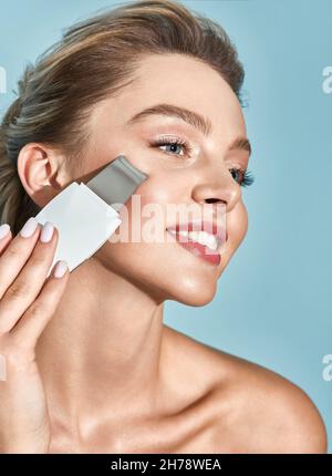 Gommage ultrasonique du visage pour une belle femme avec un épurateur ultrasonique, sur fond bleu.Nettoyage de la peau du visage, enlever les têtes noires Banque D'Images