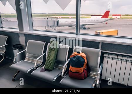 Un petit sac à dos est un bagage à main sur un banc avec vue sur la porte et un avion stationné.Les passagers montent à bord. Banque D'Images