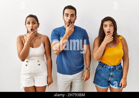 Groupe de jeunes hispaniques se tenant sur un fond isolé et regardant fasciné par la incrédulité, la surprise et l'expression stupéfaite avec les mains sur le menton Banque D'Images