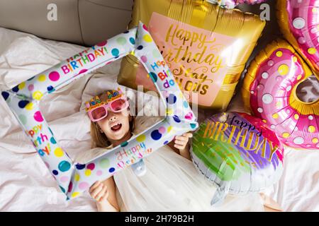 Photo d'intérieur de jolie joyeuse adorable adorable petite fille célébrant l'anniversaire de huit ans avec des ballons colorés et lumineux avec des mots d'inscription séjour Banque D'Images