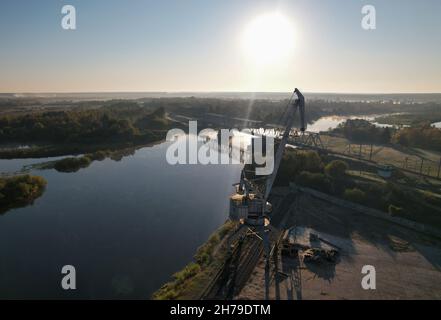 Grue portuaire inactive sur le fond d'une rivière et d'un pont ferroviaire à l'aube. Banque D'Images