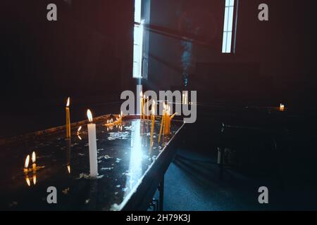 Beaucoup de bougies brûlent dans une église catholique médiévale sombre et des rayons de lumière passent par une fenêtre étroite.Le concept de foi et de rel Banque D'Images