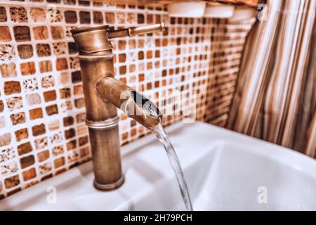 Un robinet en cuivre créatif inhabituel dans la salle de bains d'où coule un jet d'eau.Le concept de réparation et d'eau potable Banque D'Images