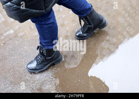 Pluie en ville, jambes de femme en bottes dans une rue avec des flaques.Les bâtiments résidentiels se reflètent dans l'eau, les femmes marchant en automne ou en hiver Banque D'Images