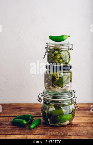 Trois jarres en verre de poivrons Jalapeno fraîchement en conserve avec herbes et ail sur une table en bois. Copier l'espace Banque D'Images