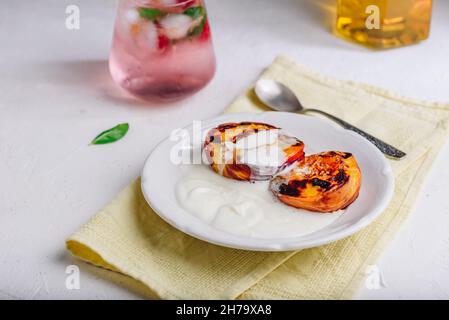 Pêches rôties au four servies avec miel et crème fouettée épaisse sur plaque blanche et verre de framboise, Mocktail à la menthe Banque D'Images