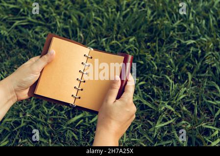 ouvrez le carnet en cuir marron dans ses mains sur un fond d'herbe verte Banque D'Images