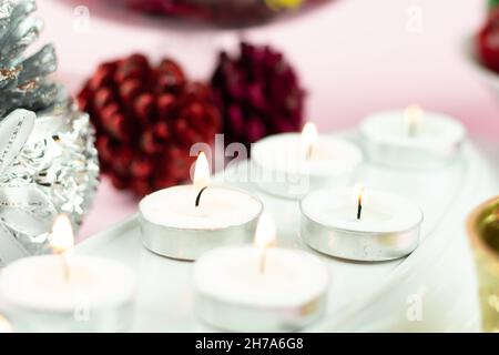 Bougies chauffe-plat blanches illuminées en rangée avec des décorations à paillettes en forme de cône de pin marron sur fond rose clair.Thème pour Joyeux Noël et Joyeux Nouveau Banque D'Images