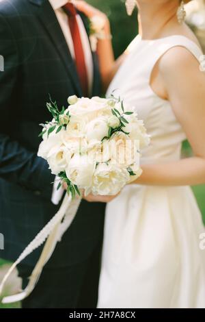 Marié dans un costume à carreaux bleus, il épouse dans une robe blanche avec un bouquet de fleurs.Gros plan Banque D'Images