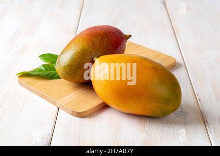 Jaune et rouge mûr juteux Palmer mangues sur une table en bois blanc.Deux savoureux fruits tropicaux de Mangifera indica.Prêt à manger de délicieuses mangues entières. Banque D'Images