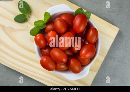 Panneau en bois avec tomates cerises sur fond gris. Fond culinaire. Banque D'Images