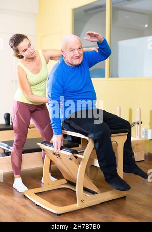 Homme âgé pratiquant des exercices de système Pilates sur la chaise unda avec entraîneur Banque D'Images