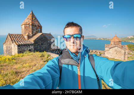 Homme voyageur solo prend photo selfie sur le fond du monastère de Sevanavank au lac de Sevan.Concept de vacances en Arménie Banque D'Images