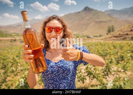 Bonne femme avec une bouteille de grappa ou de cognac sur le fond d'un vignoble.Alcools forts des cépages les plus riches Banque D'Images