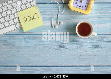 2022 écrit sur du papier jaune sur le dessus du clavier de l'ordinateur, avec des écouteurs, l'horloge et le café.Vue de dessus, espace de copie. Banque D'Images