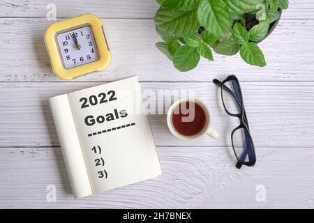 Objectifs du nouvel an 2022 sur le bureau.Vue de dessus avec café, bloc-notes, horloge, lunettes et plante verte. Banque D'Images