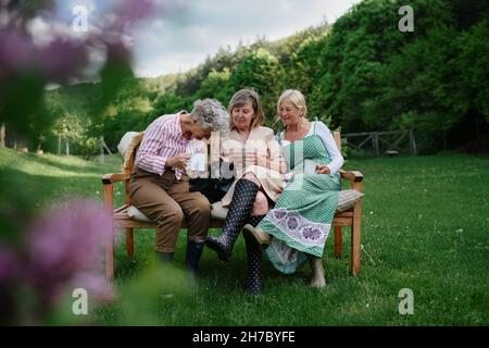 Joyeuses amies séniors assis sur le banc et buvant du thé à l'extérieur dans le jardin, en riant. Banque D'Images