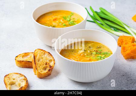 Soupe au fromage cheddar au brocoli maison avec oignons verts dans un bol blanc, fond gris.Concept de cuisine végétarienne. Banque D'Images