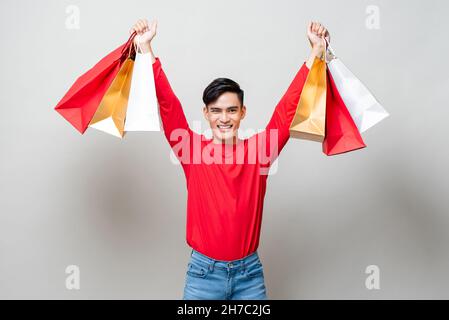 Souriant beau homme asiatique tenant des sacs de shopping isolé studio gris clair fond pour les concepts chinois de vente nouvel an Banque D'Images