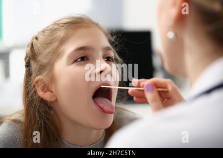 Petite fille ayant examiné sa gorge avec une cuillère spéciale chez la femme médecin à l'hôpital Banque D'Images