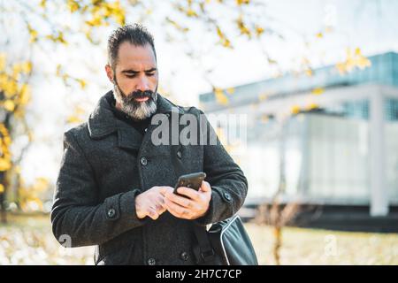 Homme d'affaires utilise un smartphone devant le bâtiment de l'entreprise dans le parc. Banque D'Images