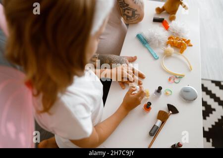 La fille peint les ongles de père de couleur jaune à la table avec des accessoires dans la chambre Banque D'Images