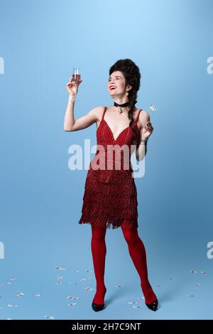 Portrait de jeune adorable magnifique femme en rouge foncé, couleur vin robe de soirée célébrant les vacances isolé sur fond bleu. Banque D'Images