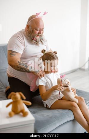 Drôle de papa fait le massage à la petite fille tenant le chien jouet et bâton magique dans la salle de séjour Banque D'Images