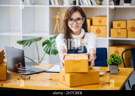 Le propriétaire de l'entreprise prend les colis et utilise un ordinateur pour vérifier les commandes en ligne pour préparer l'emballage. emballez les produits à envoyer aux clients. Banque D'Images