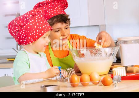 Les garçons ajoutent des œufs et du beurre pour mélanger la cuisson du bol Banque D'Images