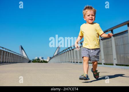 Un tout-petit garçon blond s'enjambe sur le pont piétonnier Banque D'Images