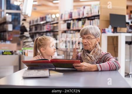 Grand-mère lit un livre à sa petite-fille à la bibliothèque Banque D'Images