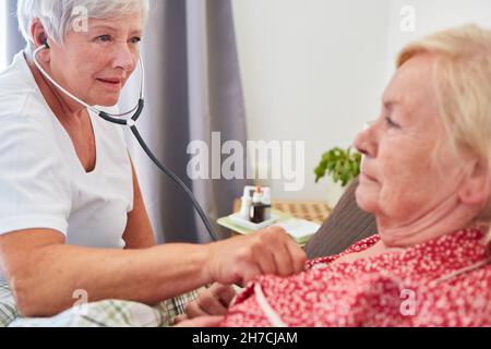 Un médecin ou une infirmière gériatrique examine une femme âgée au lit dans une maison de retraite avec un stéthoscope Banque D'Images