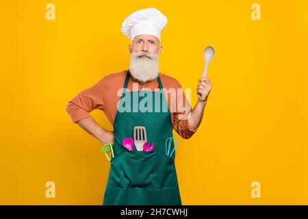 Portrait d'un sympathique homme à cheveux gris chef tenant une cuillère cuisine domestique isolée sur fond jaune vif Banque D'Images