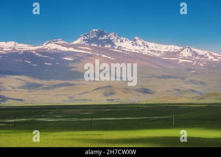 Vue sur l'ancien volcan Aragats éteint et la vallée fertile à son pied avec des terres agricoles semées au début du printemps en Arménie. Banque D'Images