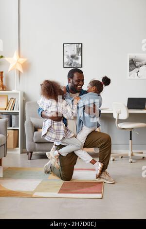 Portrait vertical complet de père afro-américain heureux jouant avec deux filles à la maison Banque D'Images