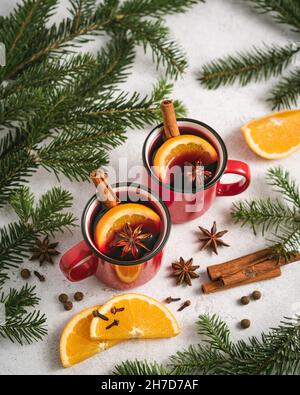 Vin chaud dans deux tasses rouges sur une table de Noël entourée de branches de sapin, d'orange et d'épices Banque D'Images