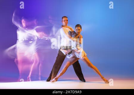 Portrait dynamique de danseurs gracieux, homme et femme flexibles dansant danse de salle de bal isolé sur fond bleu dégradé violet dans lumière mélangée néon Banque D'Images