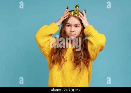 Portrait de petite fille princesse debout et porter couronne de diadem doré avec le sourire, regardant l'appareil photo, portant jaune style décontracté pull.Studio d'intérieur isolé sur fond bleu. Banque D'Images