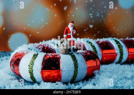 gros plan d'un père noël miniature portant un sac avec des cadeaux sur une fausse canne à sucre et une fausse neige tombant sur lui Banque D'Images