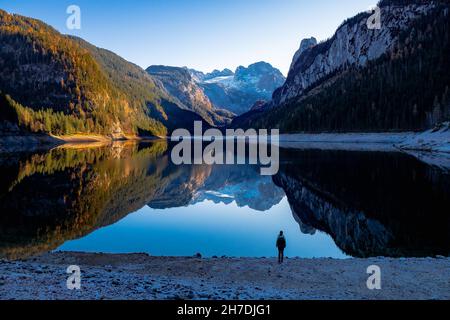 Femme regardant la chaîne de montagnes 'Gosaukamm' et le glacier de Dachstein se reflétant sur le lac de Gosausee, Gosau, Salzkammergut, OÖ, Autriche Banque D'Images