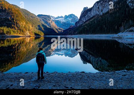 Femme regardant la chaîne de montagnes 'Gosaukamm' et le glacier de Dachstein se reflétant sur le lac de Gosausee, Gosau, Salzkammergut, OÖ, Autriche Banque D'Images