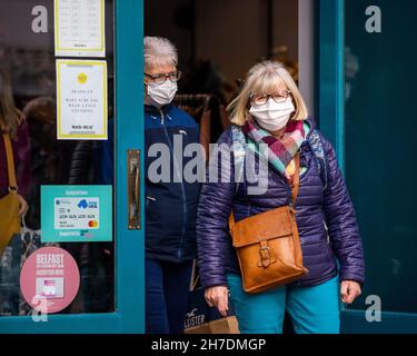 Deux femmes portant un masque quittent le magasin White Stuff de Belfast, en passant devant un panneau informant tous les clients qu'elles doivent porter un couvre-visage. Banque D'Images