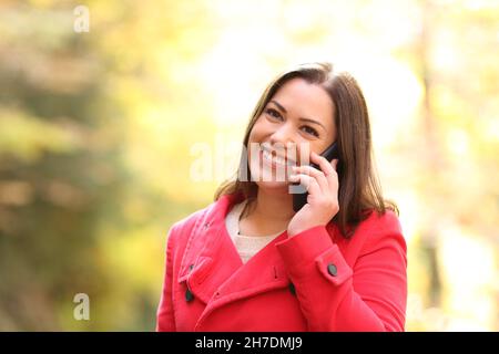 Une femme heureuse en rouge parlant sur un téléphone mobile marchant dans un parc en hiver Banque D'Images