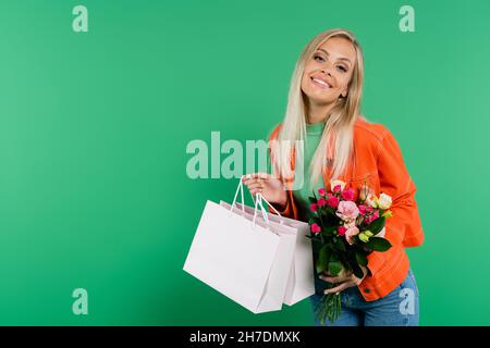 une femme joyeuse avec des sacs de shopping et un bouquet souriant à l'appareil photo isolé sur le vert Banque D'Images
