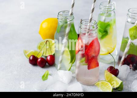 Beaucoup de bouteilles avec limonade d'été rafraîchissante avec citron vert, fraise, cerise, concombre et glace sur fond de béton gris Banque D'Images