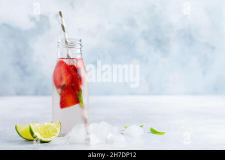 Limonade d'été avec glace, fraises, menthe et lime dans une bouteille et un tube en papier sur fond gris en béton. Concept de boisson saine Banque D'Images