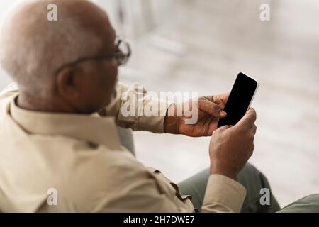 Homme afro-américain senior utilisant le téléphone avec écran vide à l'intérieur Banque D'Images
